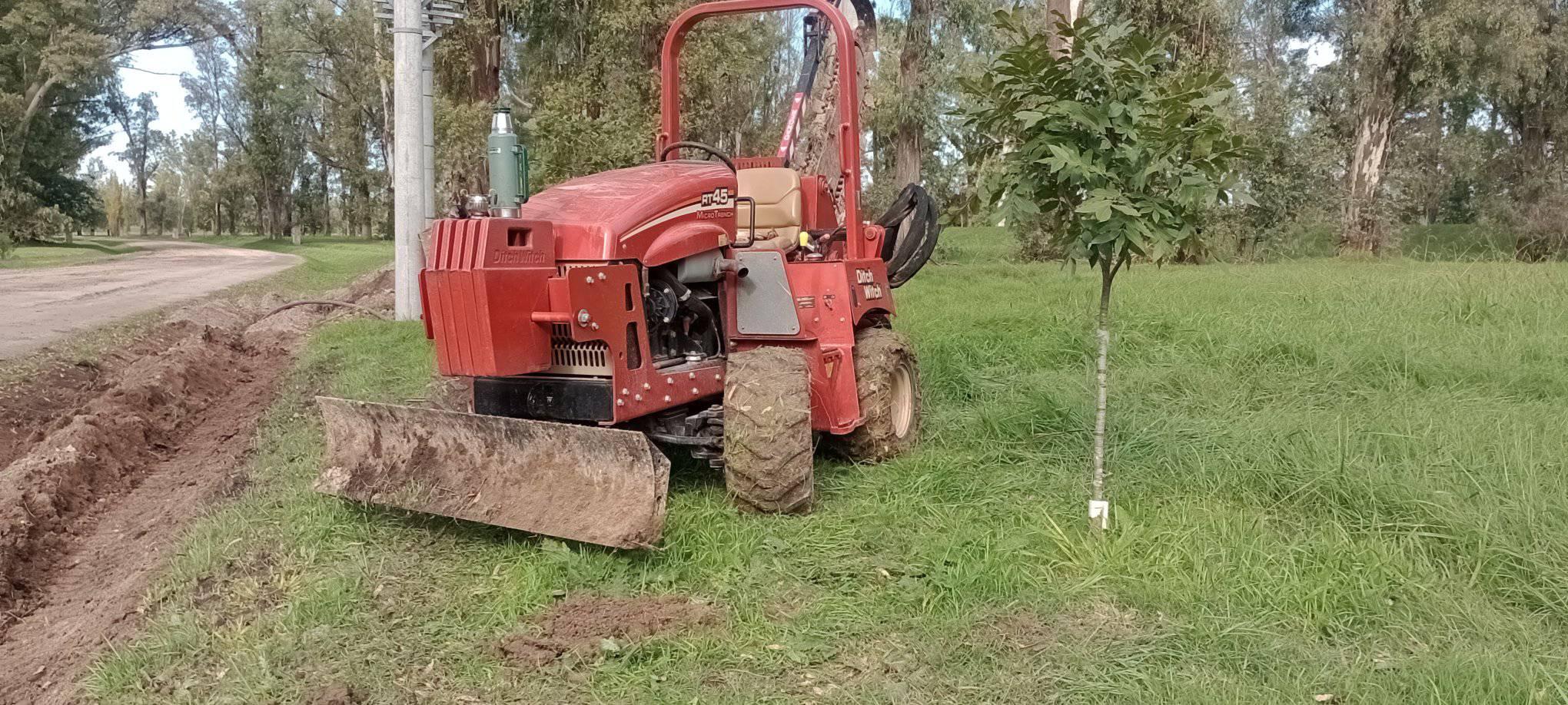 Zanjadora abriendo una zanja junto a un camino arbolado